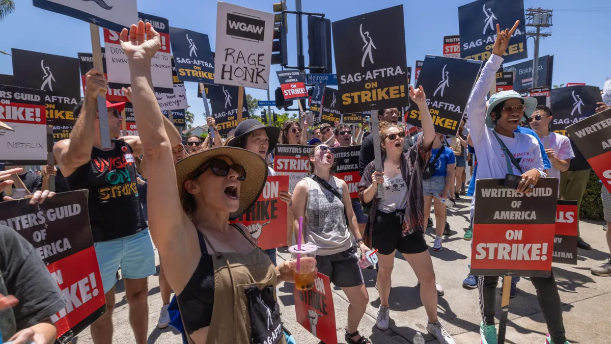 A crowd of acting and writing strikers carry picket signs.