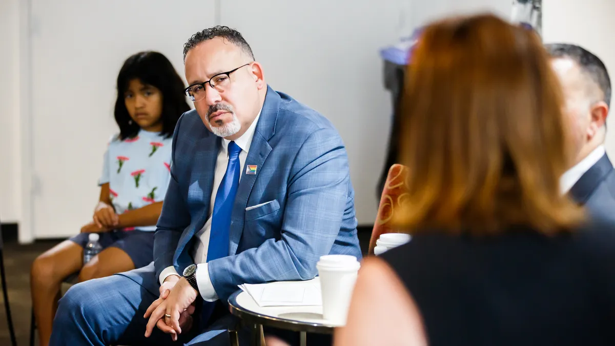 Miguel Cardona sits surrounded by students and others