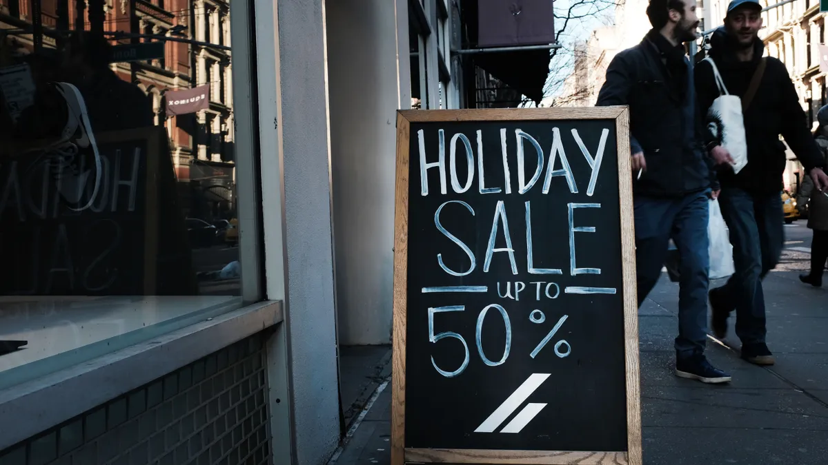 A sign advertises a holiday sale as people walk by.