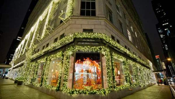 Exterior view of the corner of a department store in the evening, covered in white Christmas lights.