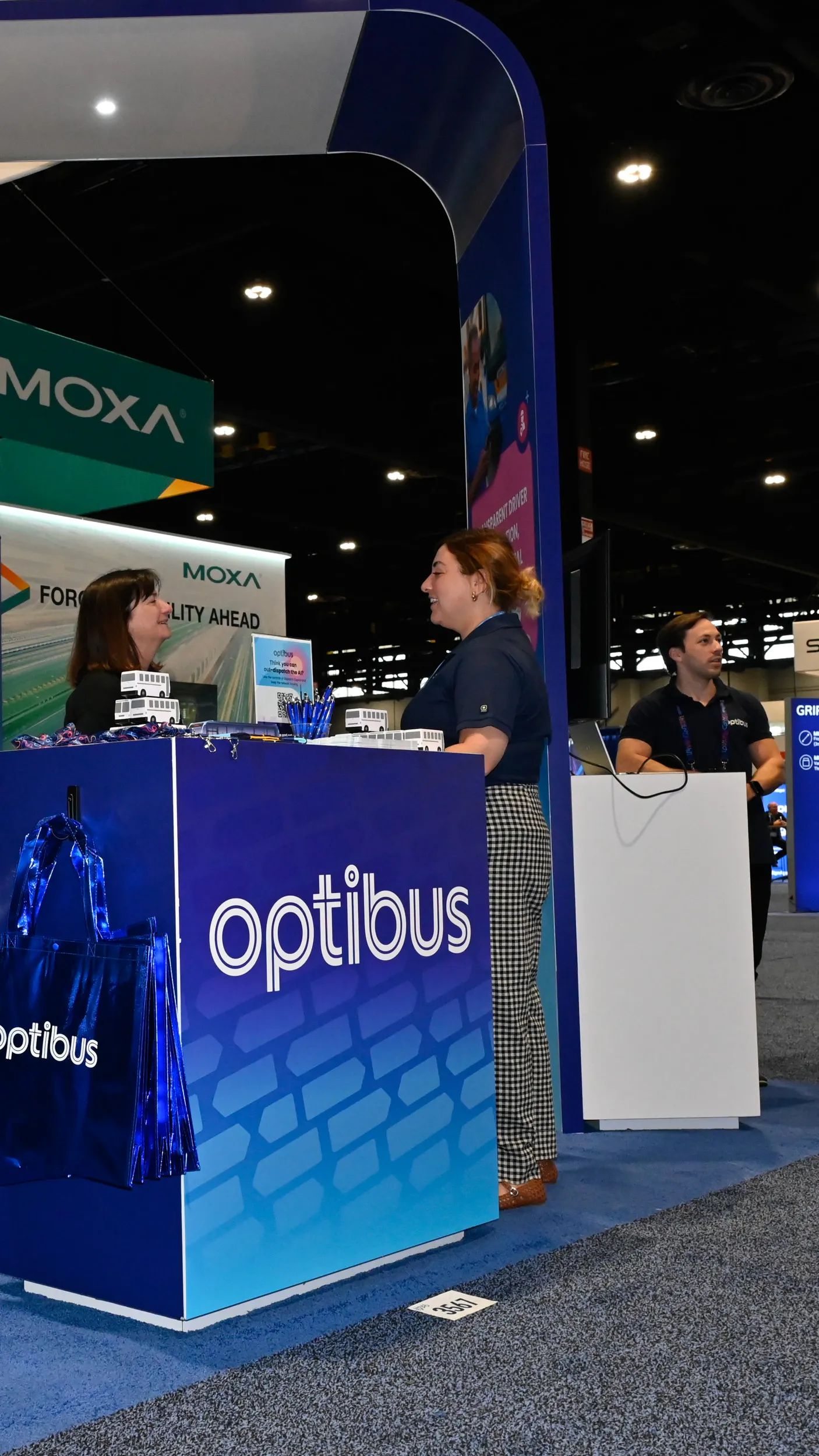 Three people at an exhibit booth labeled Optibus.