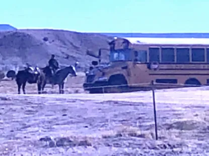 A pair of horses are shown next to a school bus and their student owners, who traveled on horseback to get meals and access the internet in Arizona's Chinle Unified School District during COVID-19.