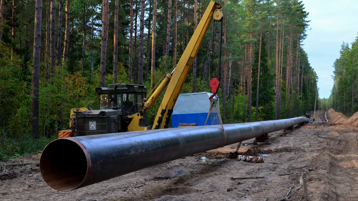 Pipe-laying crane lowers a section of pipe into a trench.