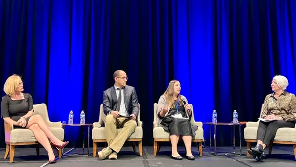 Four people sit on chairs on a stage. One person has a microphone and is speaking.