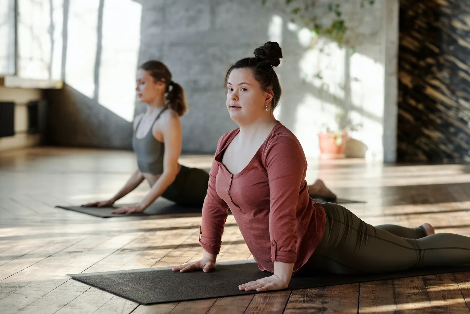 Two people, including a person with Down syndrome, do yoga together in a studio