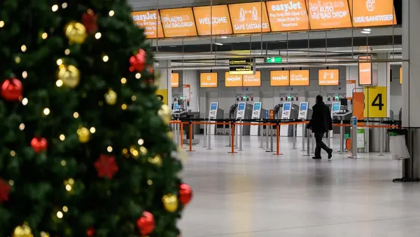 A person walks through an airport with a Christmas tree in the foreground.