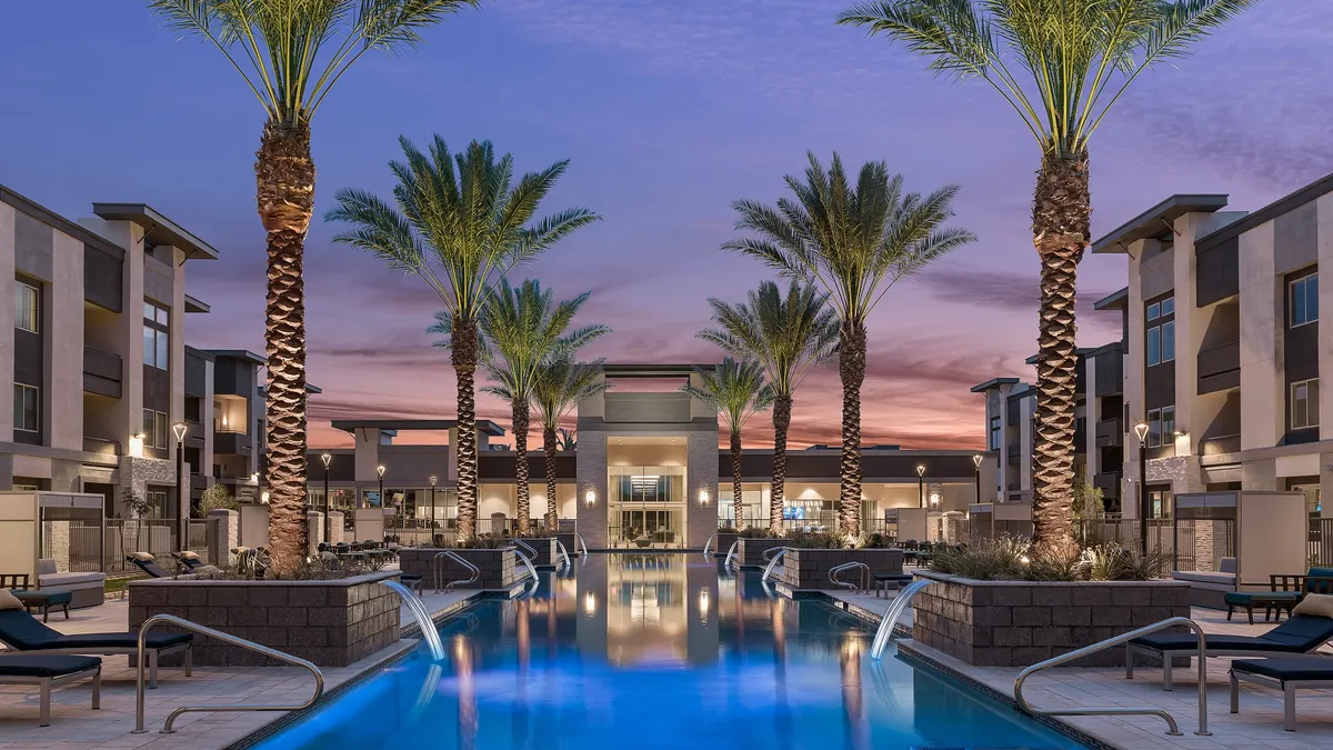 A pool area with waterfalls, surrounded by palm trees, in the early evening.