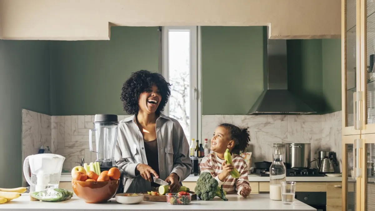 A Mother Preparing Lunch In The Kitchen And Smiling With Her Little Daughter