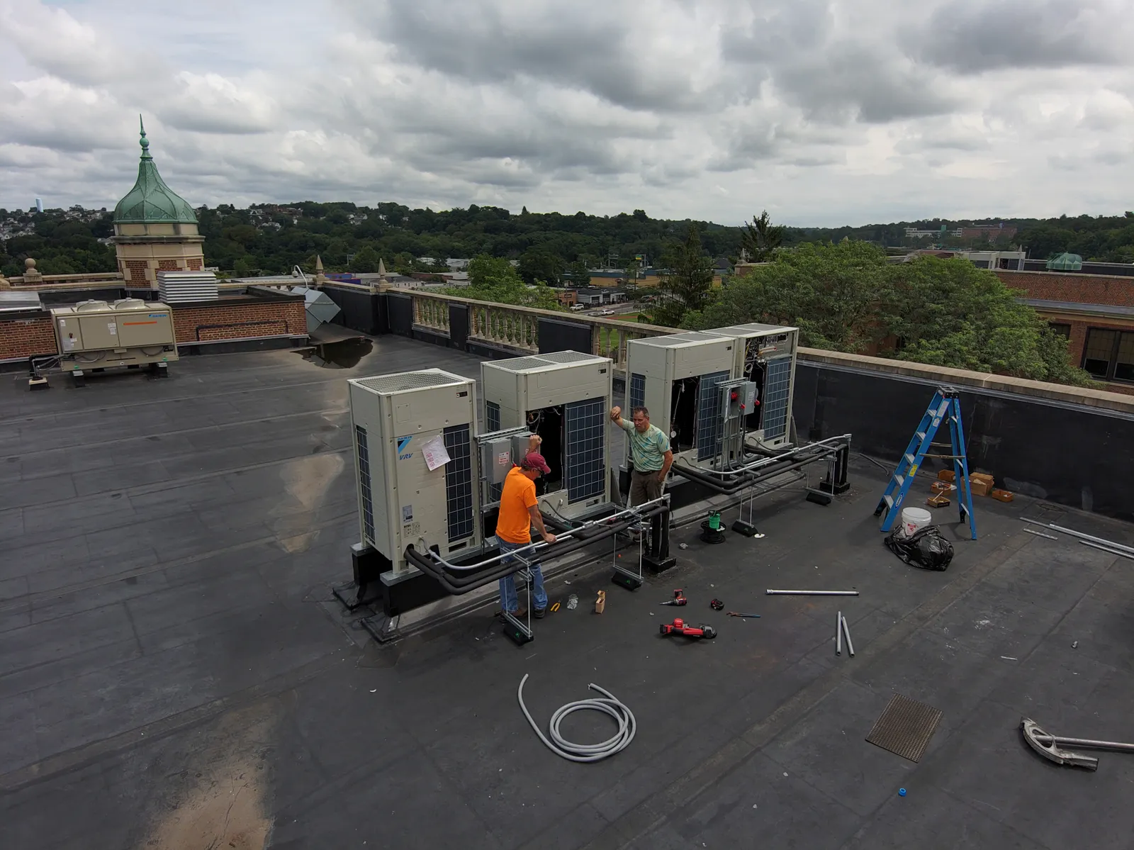 Two workers are on a roof of a school with a new condenser for an HVAC system.