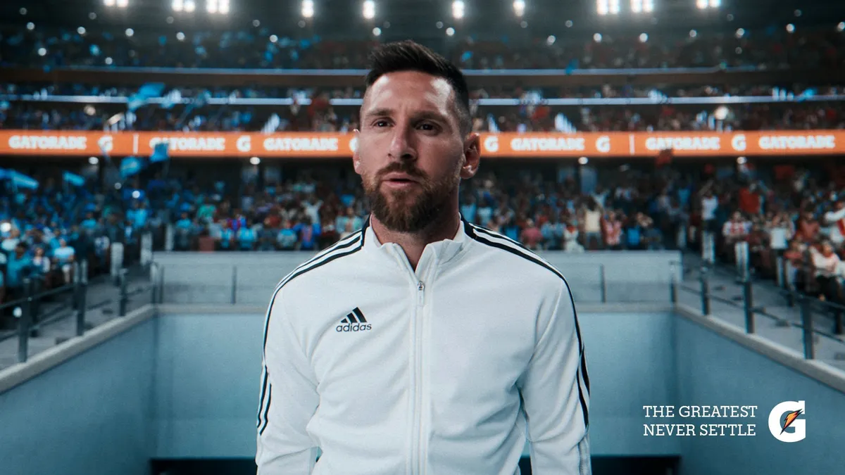 Lionel Messi wears a white Adidas jacket and stands before a crowd.