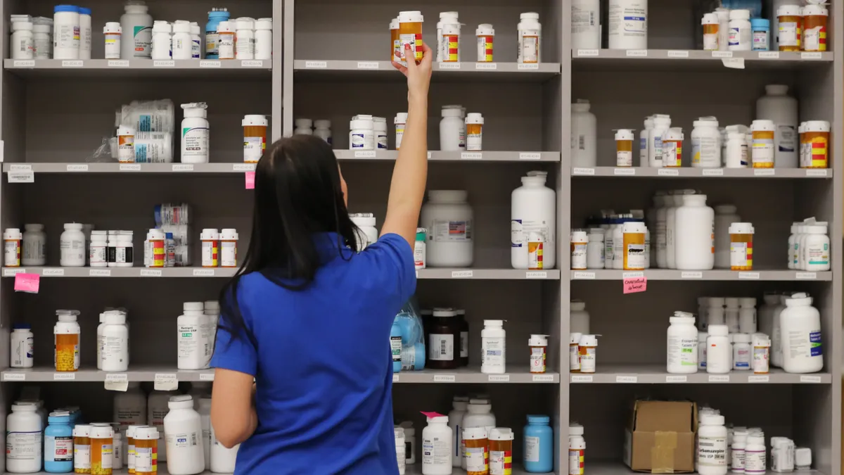 Pharmacy technician grabs a bottle of drugs of a shelf.