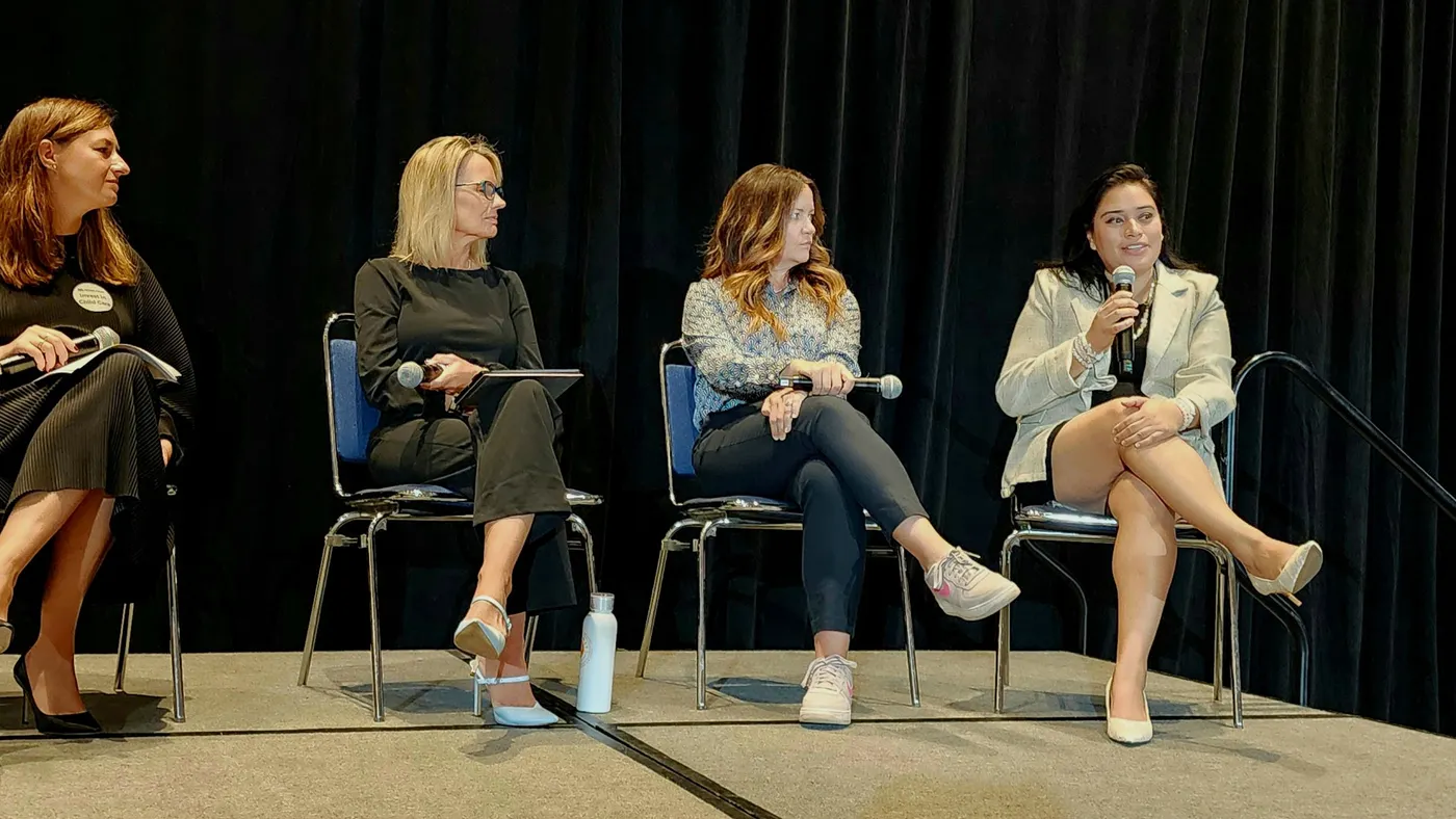 Four women sitting in chairs next to each other, and each holding their own microphone.