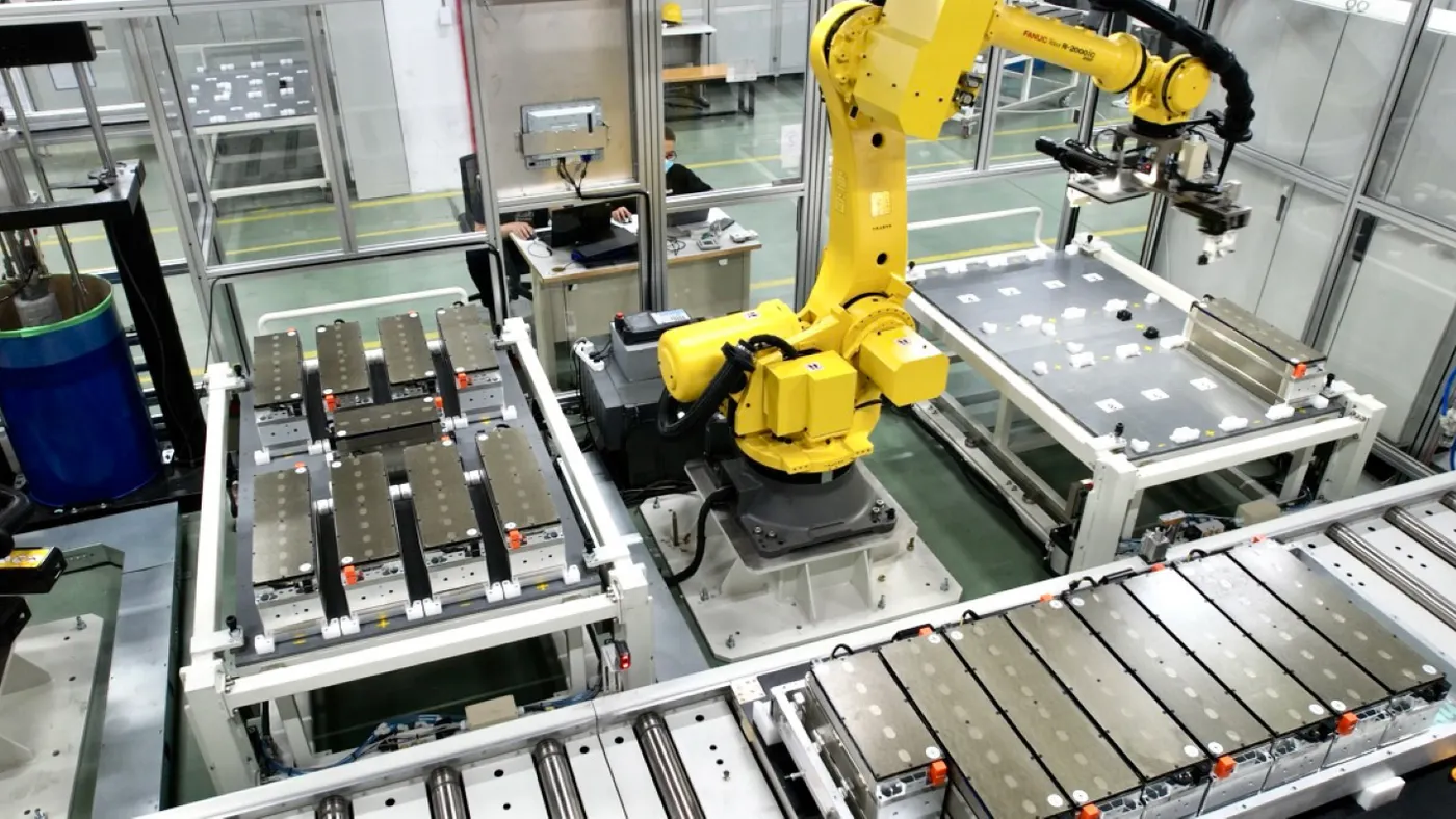 A yellow robot working on a silver battery cell in an e-Storage facility.