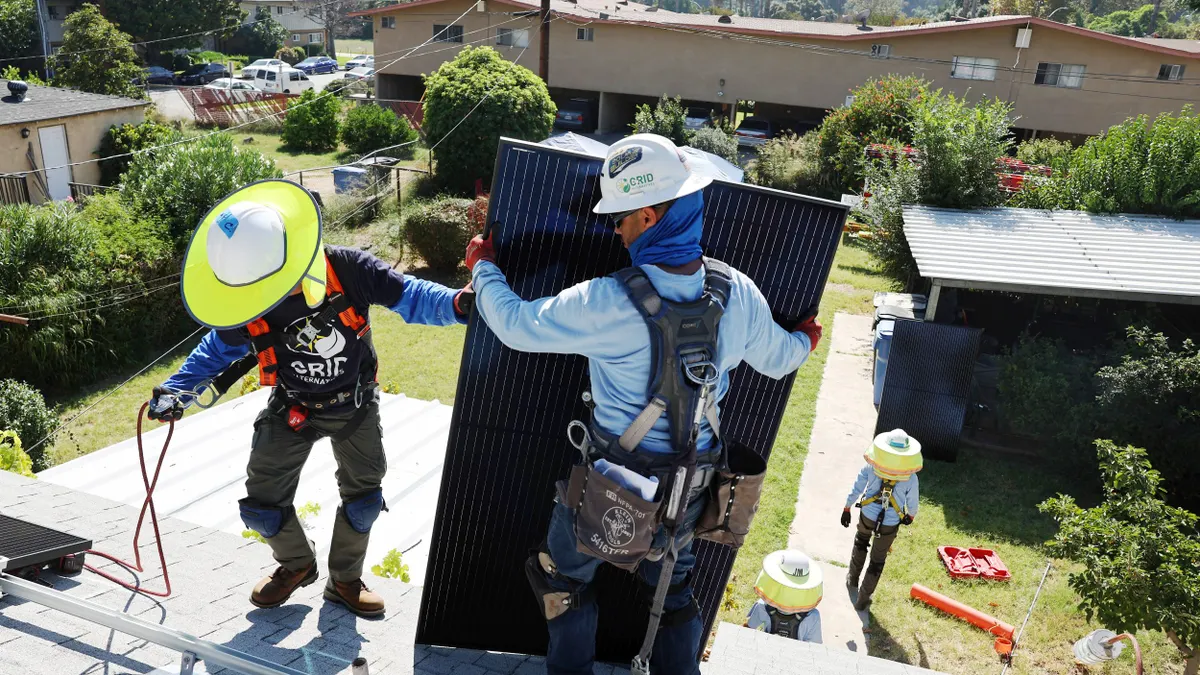 Workers install solar panels on the rooftop of a home.