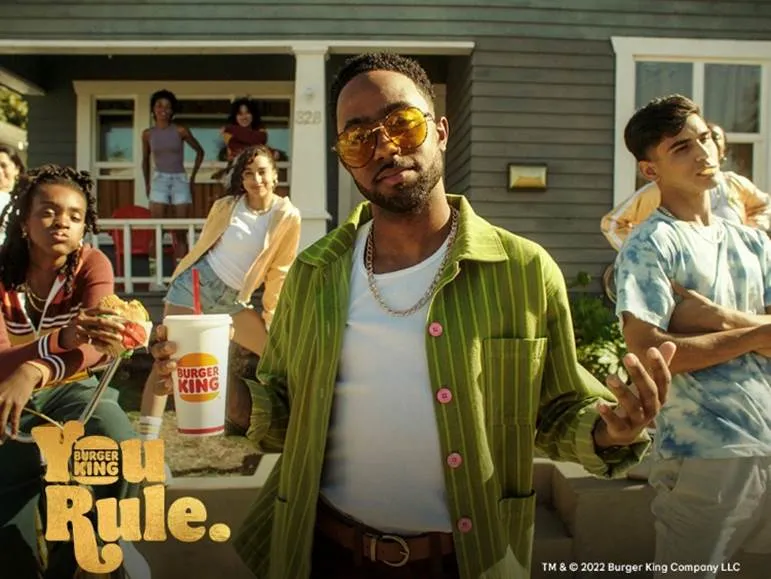 A group of young people eat Burger King in front of a grey house.