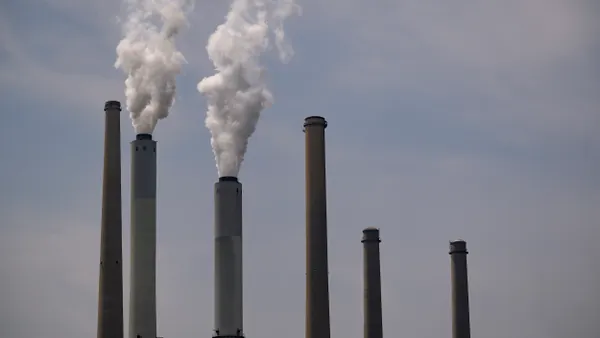 White smoke streams from two of six smokestacks against a blue sky.