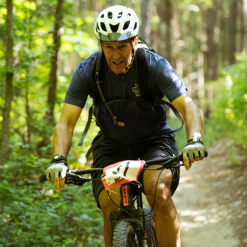 A man wearing a helmet riding a bicycles along a forest trail.