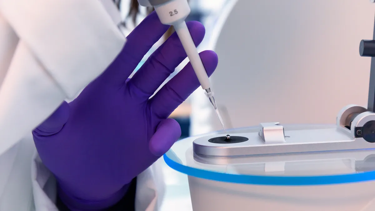 A person uses a syringe to fill a well plate under a microscope.
