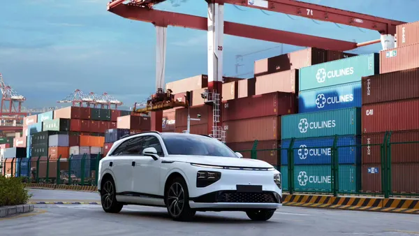 A white G9 electric SUV from China-based automaker Xpeng parked at a port with shipping containers in the background.
