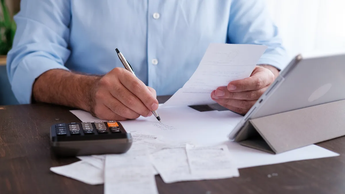 Person in blue shirt holding a pen with a calculator and papers in front of them.