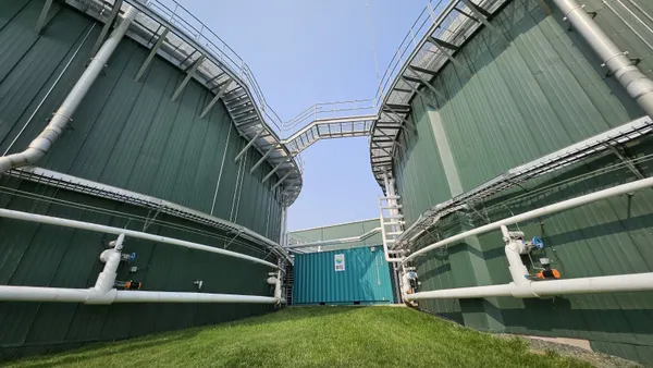 Two massive cylindrical tank buildings are connected by pipes and encircled by catwalks. A building connecting the two has a sign with the "BTS Bioenergy" logo.