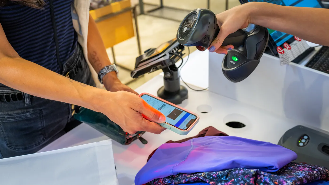 A person is seen holding a cell phone to be scanned by another person working at a store.