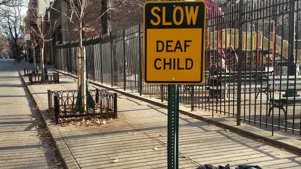 Yellow sign that says "Slow Deaf Child" on a city street