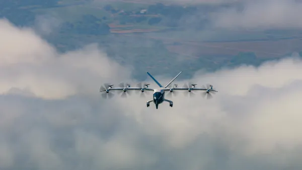 An aircraft with multiple rotors in flight among blue skies and clouds.