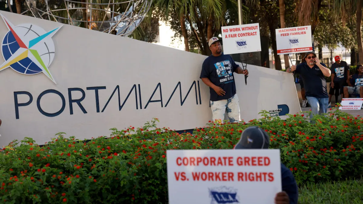 Dockworkers hold picket signs as they strike in front of a port.