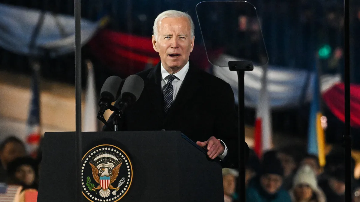 Joe Biden stands in front of a podium, speaking to a crowd in Warsaw, Poland