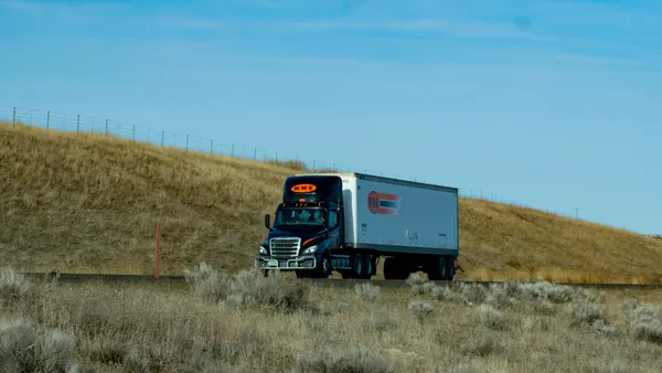 A Midwest Motor Express semi-truck traveling on a road with an almost completely barren hillside and blue sky in the background.