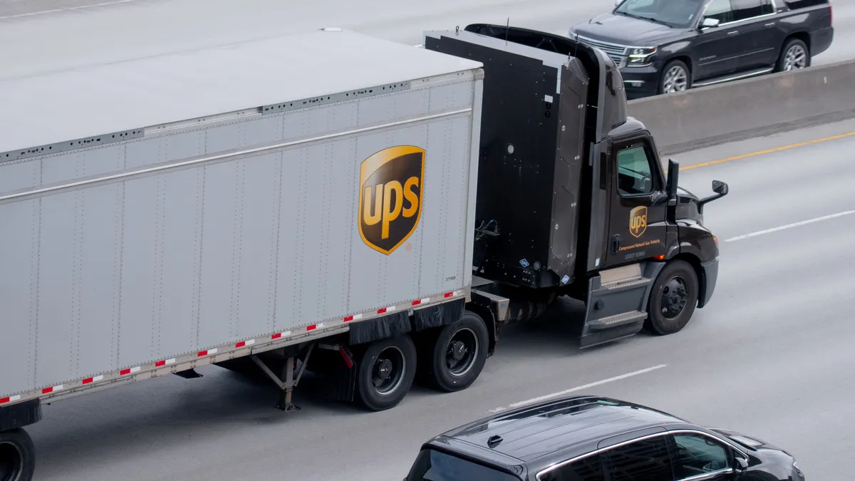 A UPS semi-truck and passenger vehicle go in opposite directions on a highway, separated by a median barrier.