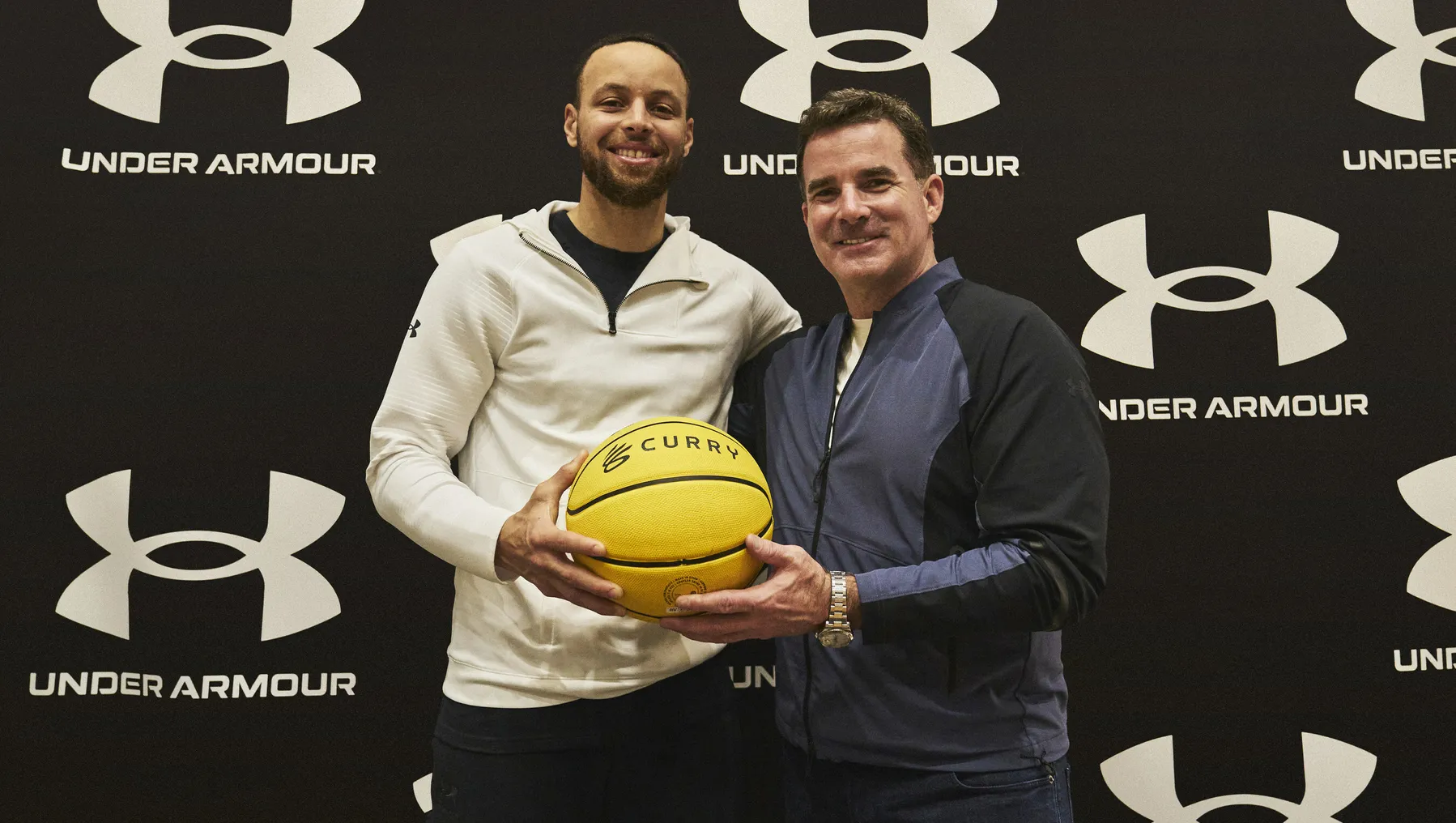 Basketball star Steph Curry holds a basketball with Under Armour founder Kevin Plank.