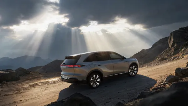 A Buick Electra E7 SUV driving on a mountain road with sunlight streaming through clouds in the background.