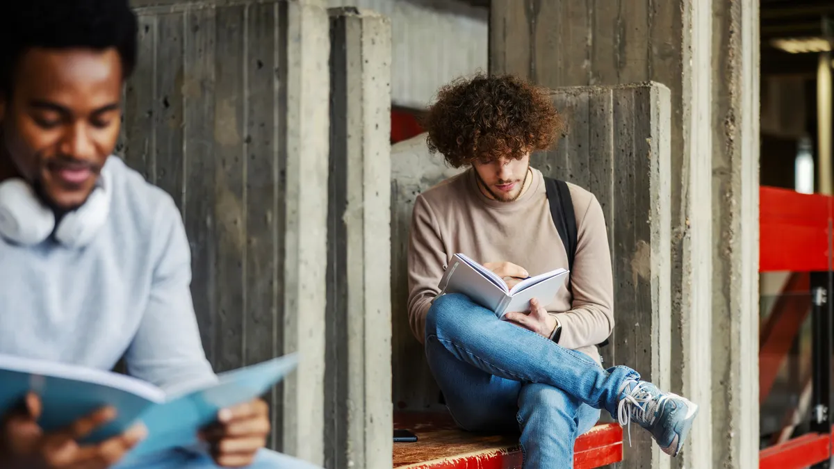 Two people sit on different benches while reading.