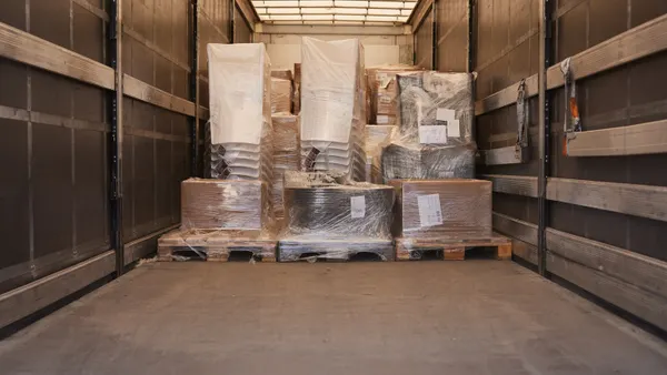 A partially full semi-truck seen from the rear doors containing pallets loaded with plastic covered cargo.