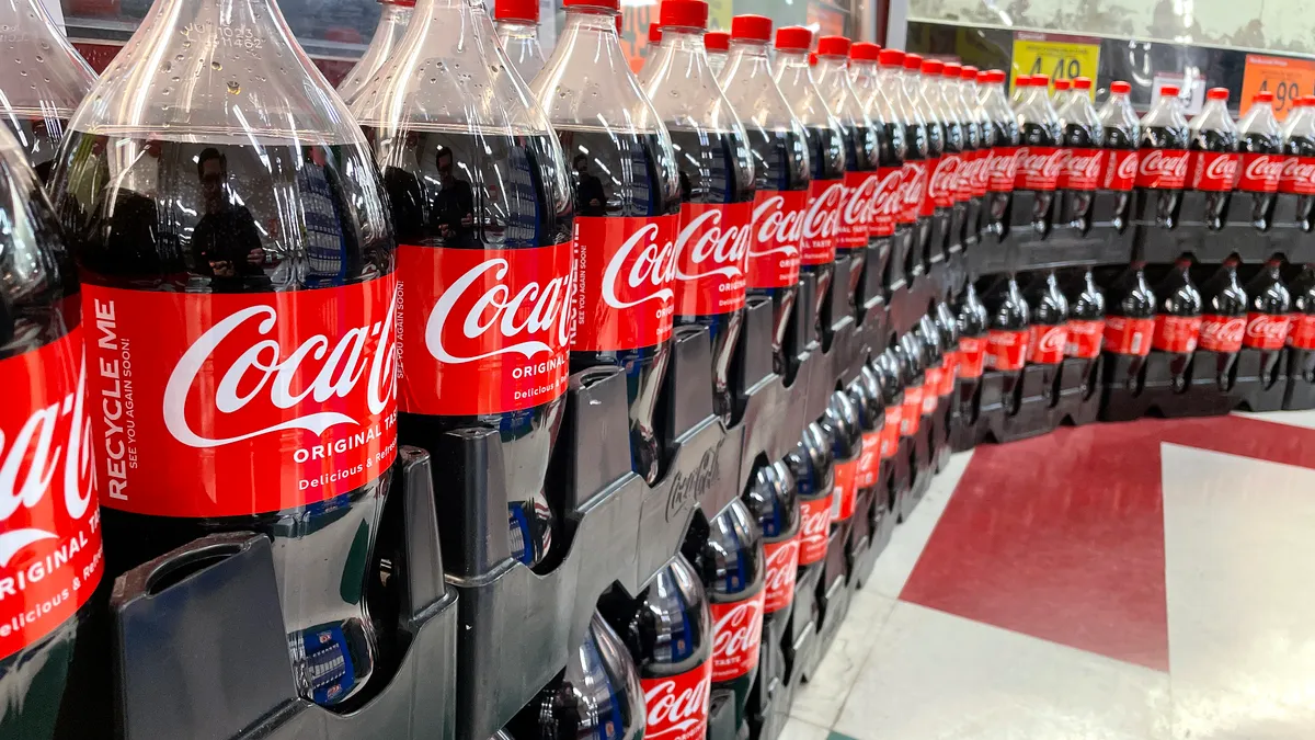 A row of Coca Cola bottles stand in containers in a grocery store.