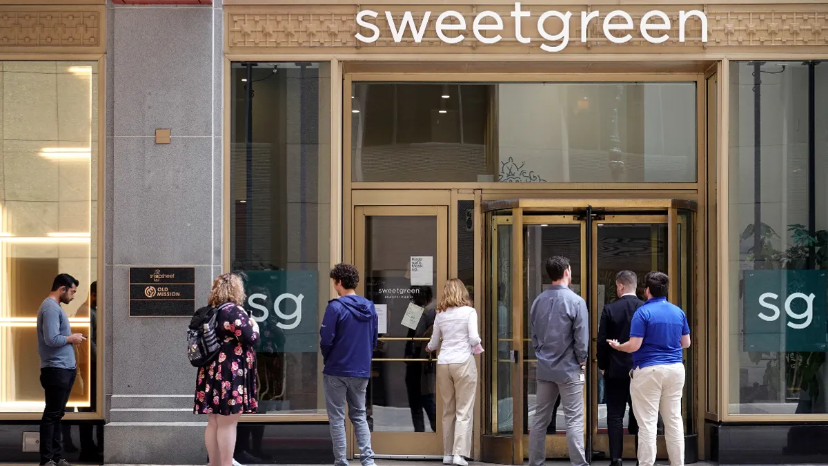 People wait in line to enter a building with a sweetgreen logo at the top.