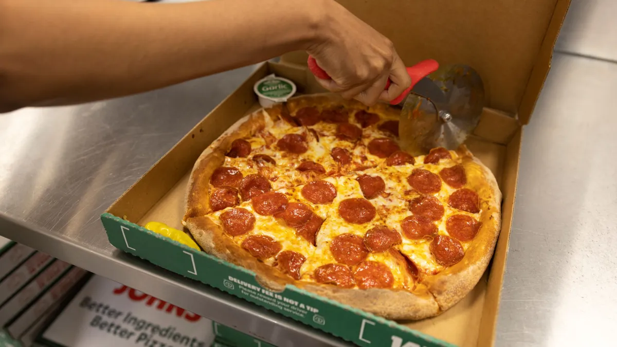 A Papa Johns' employee cuts pizza after preparing it.