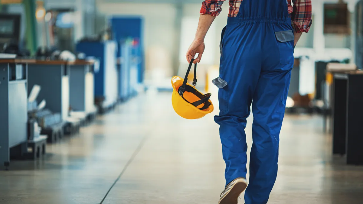 The back of a factory worker carrying their hardhat in hand and leaving the plant.