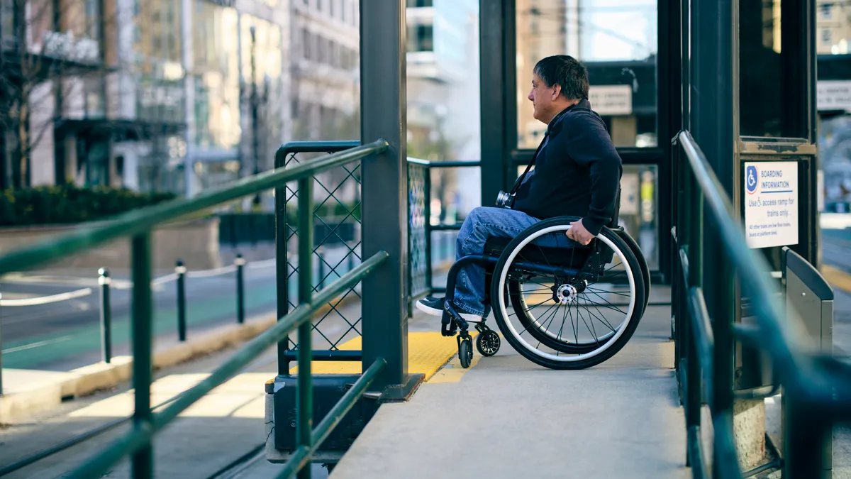 Man in a wheelchair on a ramp at an urban train station.