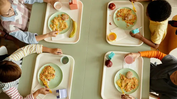 A view from above of elementary school students sitting together at a large table eating lunch in a cafeteria.