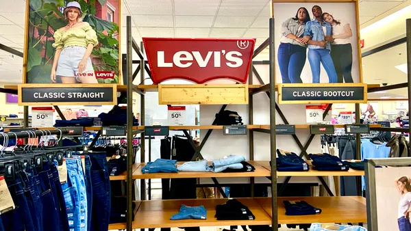 A store display with a red Levi's sign includes jeans in various shades of blue, folded on shelves and hanging on racks.