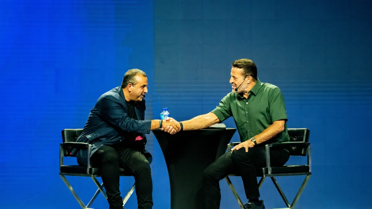 Sam Nazarian and Tony Robbins shake hands while sitting at a table.