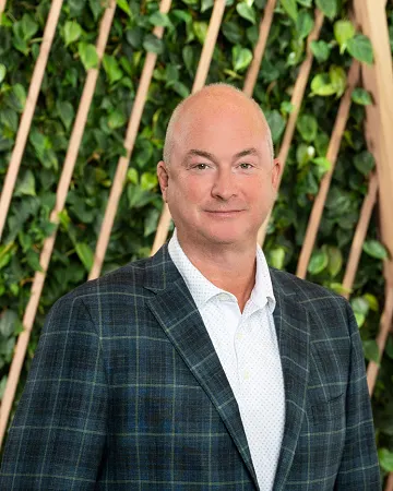 A headshot of a white man in a plaid suit.