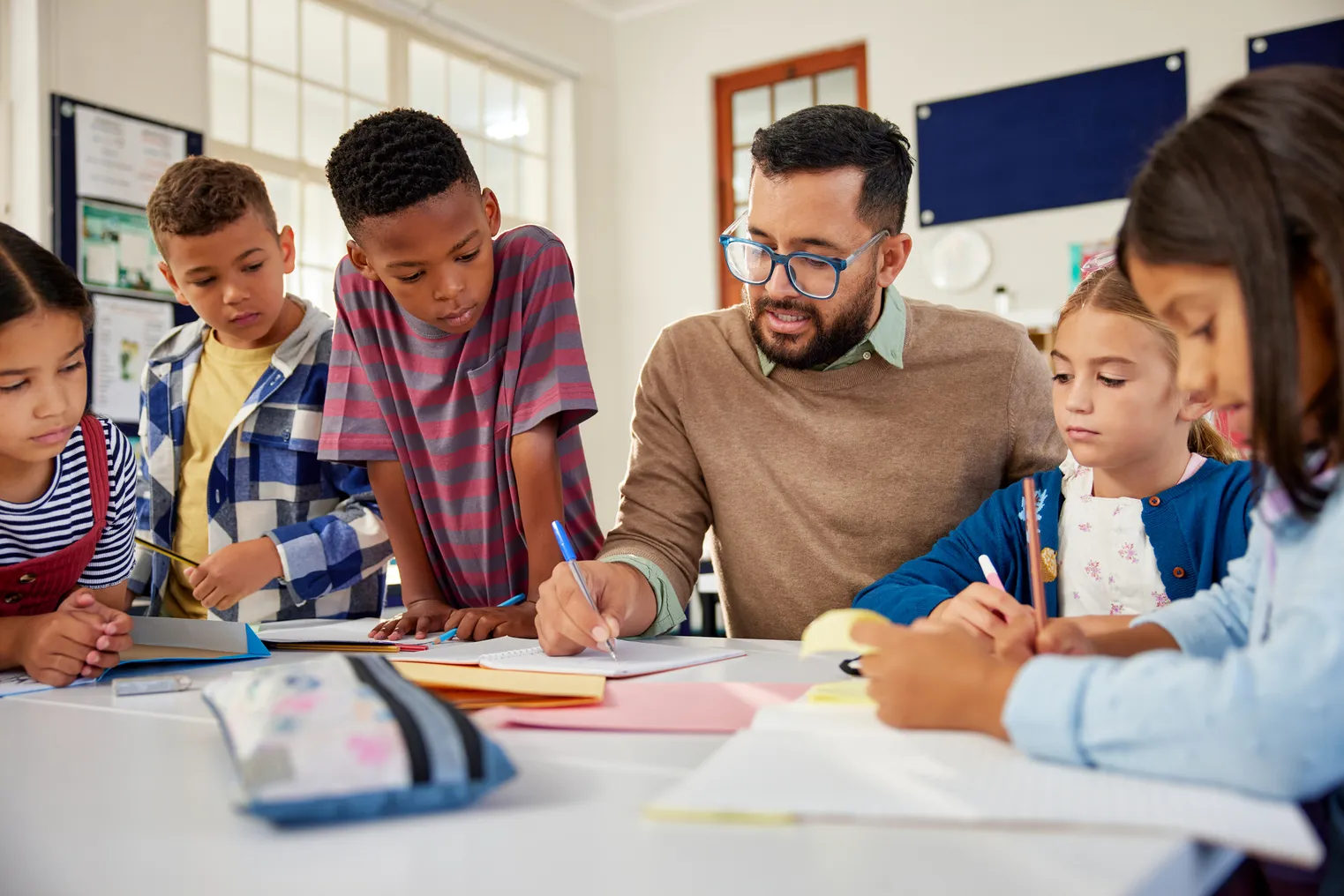 Young school teacher helping elementary students while writing in notebooks