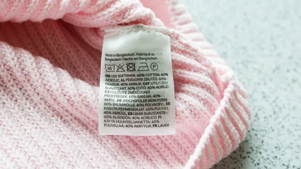 A white label with care instructions attached to a baby pink sweater-like clothing.
