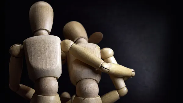 A wooden mannequin with arm around another wooden mannequin.
