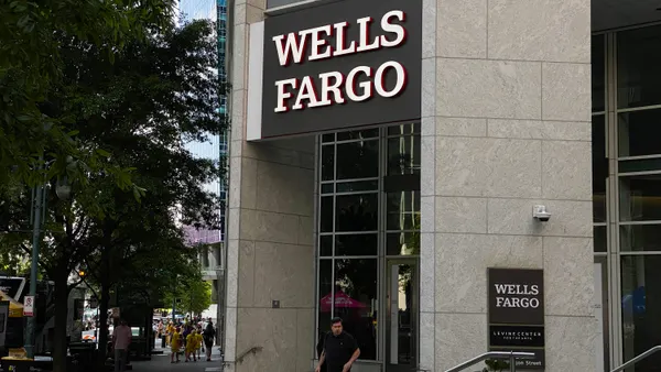 A person walks out of the entrance way of a stone and glass building that has a "Wells Fargo" sign above the street corner entrance.