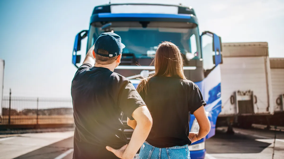 Two professional truck drivers stand in front of the big truck. They talk and perform a technical inspection of the vehicle before next drive. Professional transportation concept.